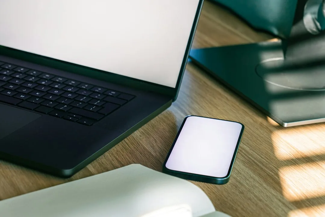 Điện thoại màn hình trống đặt cạnh laptop trên bàn gỗ